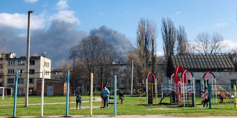 ft_image_krem_960 Adults and children in a play area look upwards at a large black smoke plume rising from behind nearby buildings.