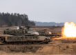 Two Abrams tanks on a firing range fire producing large bursts of flame during a NATO exercise in 2024.