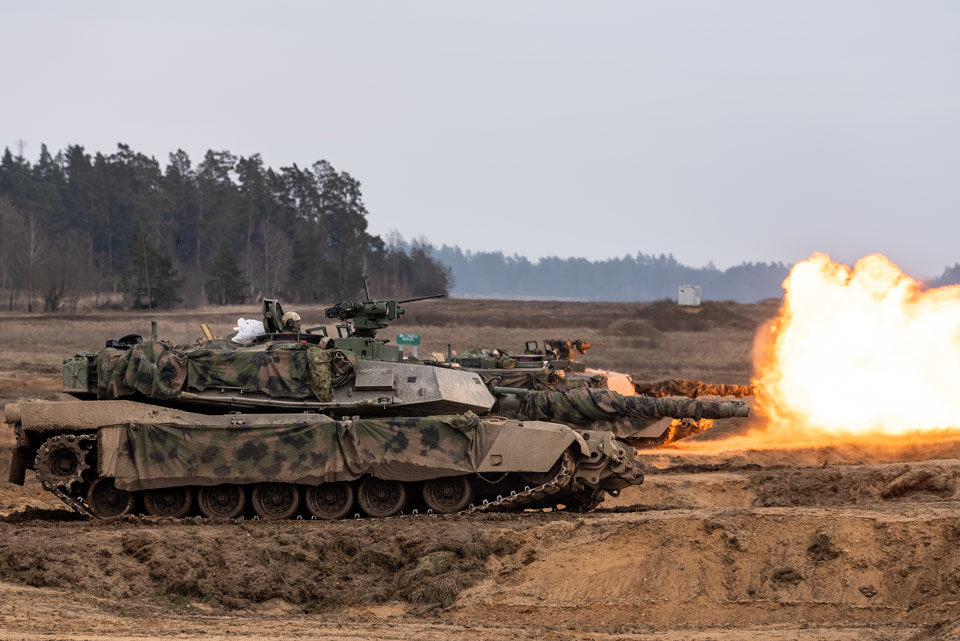 Two Abrams tanks on a firing range fire producing large bursts of flame during a NATO exercise in 2024.