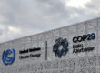 The entrance to the building that will be home to COP29 showing the UNFCCC logo and COP29's logo against a grey sky.