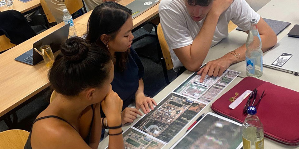 remolte-sensing-exercise_960 Three students sit at a desk looking at blown up satellite images of facilities in Ukraine, they are deep in conversation.