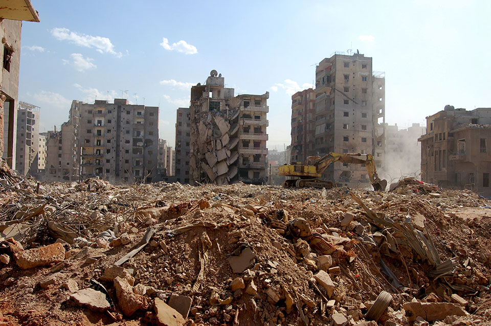 In the foreground piles of brownish rubble and debris, behind several bomb damaged tower blocks can be seen, most around 7 stories and all showing high levels of damage - concrete shells.