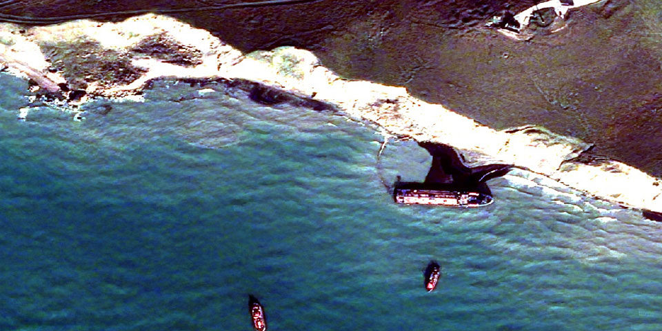 ft_image_960 Satellite image of one of the wreck sites. Most of the image is the sea in shades or dark to mid blue, in the top right a coast line and white cliffs, in the far right of the image the lozenge like shape of a small tanker can be seen, just offshire, between it and the cliffs is a black slick of oil. Three smaller craft are offshore nearby.