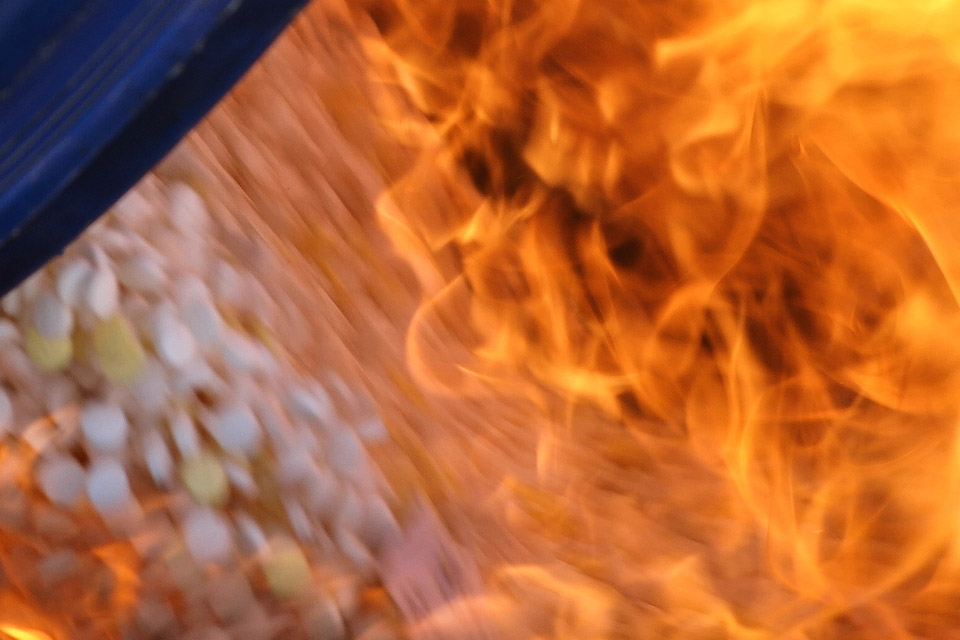 A blurred close up image shows white pills being consumed by orange flames.