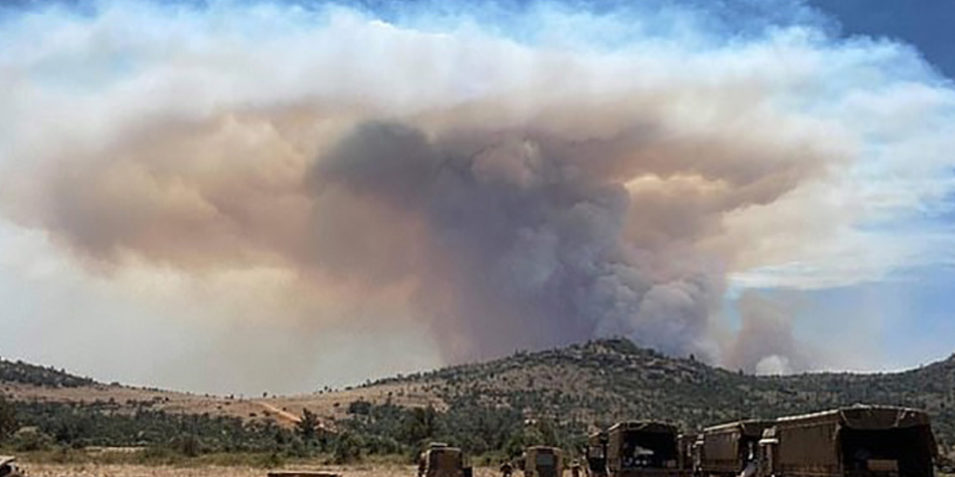 conservancy-fire_960 UK military personnel look on as a huge smoke plume rises from a distant ridgeline, a selection of army trucks and off road vehicles are in the foreground.