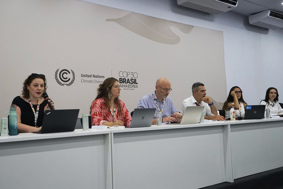 Six panellists sit behind laptops in front of a grey wall bearing the logo of the UNFCCC and COP30.