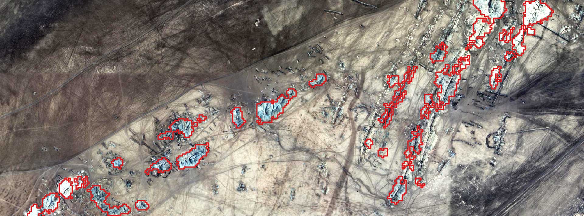 A satellite image of a gold producing area of Sudan, the landscape is browny cream with complex surface geology. Small areas are picked out in red, corresponding to gold mine areas that have been detected.