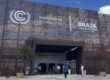 The entrance to the COP3 exhibition centre in Belem, the large doorway is towered over by a metal mesh backdrop with the event and UNFCCC logos on them.