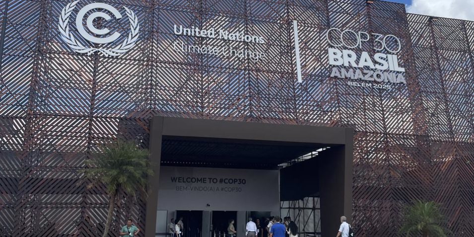 The entrance to the COP3 exhibition centre in Belem, the large doorway is towered over by a metal mesh backdrop with the event and UNFCCC logos on them.