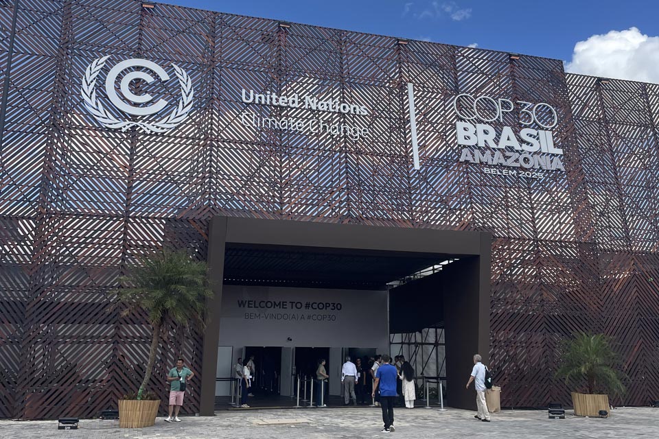 The entrance to the COP3 exhibition centre in Belem, the large doorway is towered over by a metal mesh backdrop with the event and UNFCCC logos on them.