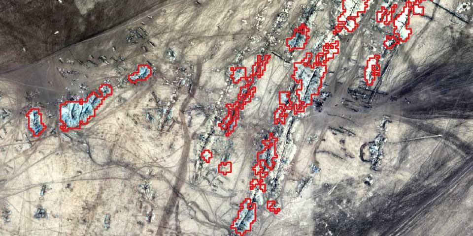 A satellite image of a gold producing area of Sudan, the landscape is browny cream with complex surface geology. Small areas are picked out in red, corresponding to gold mine areas that have been detected.