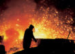 Metallurgist working by the blast furnaces in Třinec Iron and Steel Works.. A man in protective clothing is silhouetted against orange and yellow sparks and glow from the furnace.