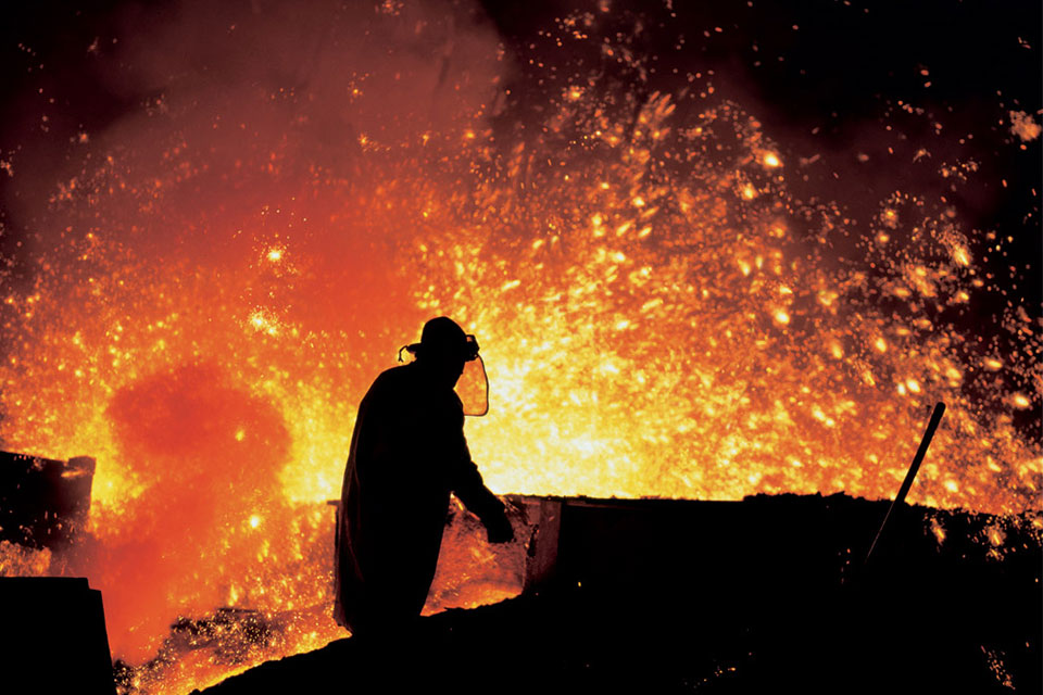 Metallurgist working by the blast furnaces in Třinec Iron and Steel Works.. A man in protective clothing is silhouetted against orange and yellow sparks and glow from the furnace.