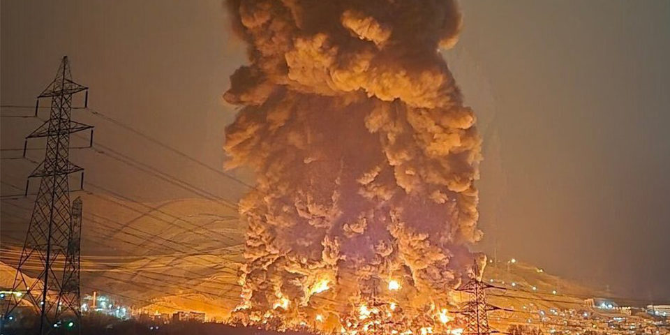 Tehran_oil_fire_960 Nighttime image, a huge fire a smoke plume can be seen, glowing orange as a column of black smoke rises into the sky.