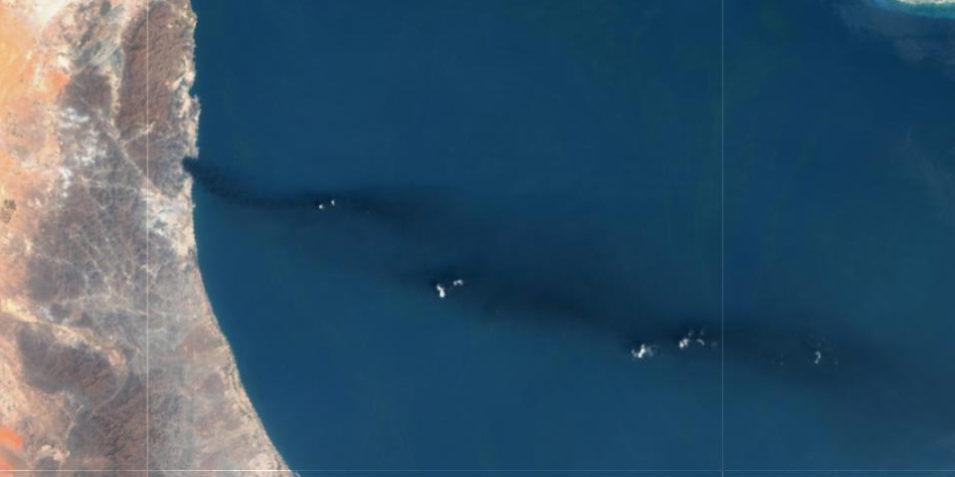 Most of the image is the deep blue of the Persian Gulf, to the left a strip of brown and orange land curves downwards, a third of the way down a dark plume is visible stretchin all the way across the sea to the right of the image.