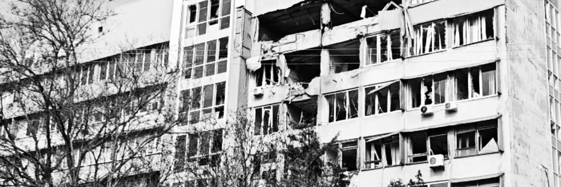 A high contrast black and white image shows blast damage to the top four floors of a large university building.
