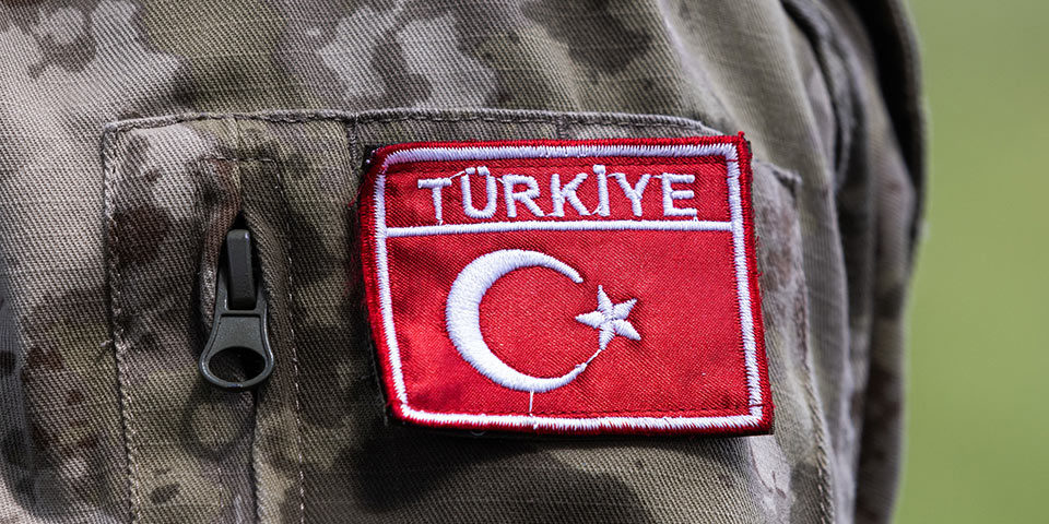 Close up of a badge on a soldier's mottled camouflage uniform, The red rectangle reads Turkiye and features the flag's crescent moon and star picked out in white embroidery.