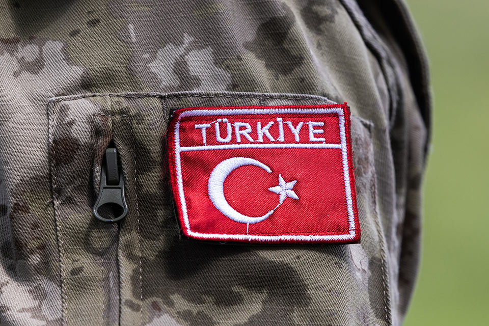 Close up of a badge on a soldier's mottled camouflage uniform, The red rectangle reads Turkiye and features the flag's crescent moon and star picked out in white embroidery.
